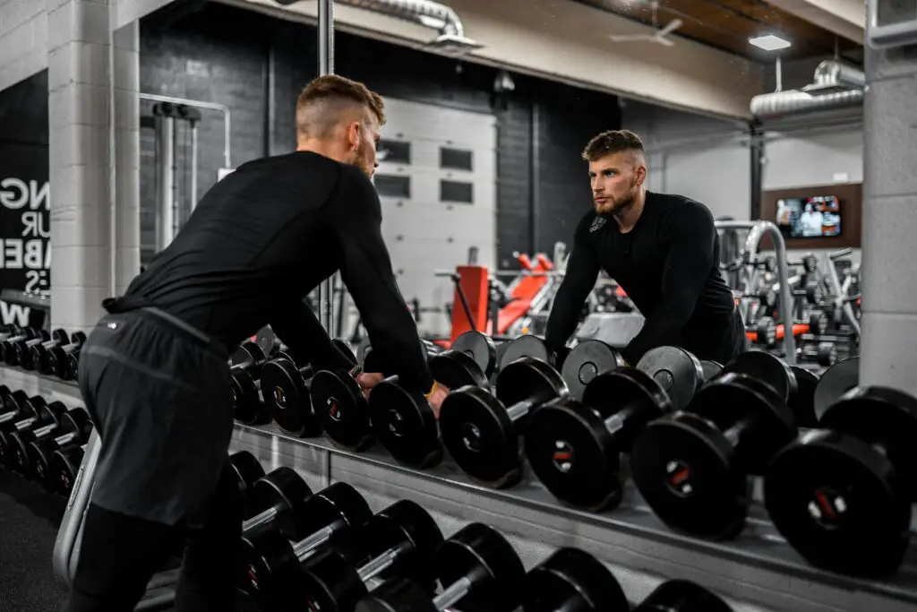 man at dumbbell rack picking up dumbbell