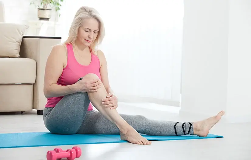 older woman bending knee with pink shirt and gray yoga pants